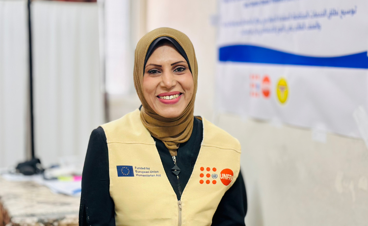 A woman in a UNFPA vest and mustard-coloured head covering smiles into the camera